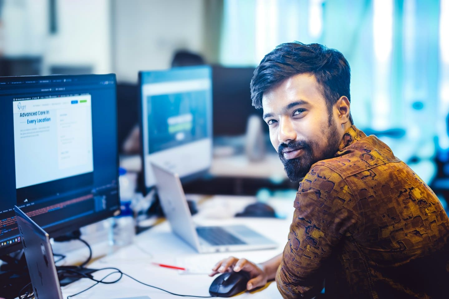 Smiling man works at a desk with multiple computers.