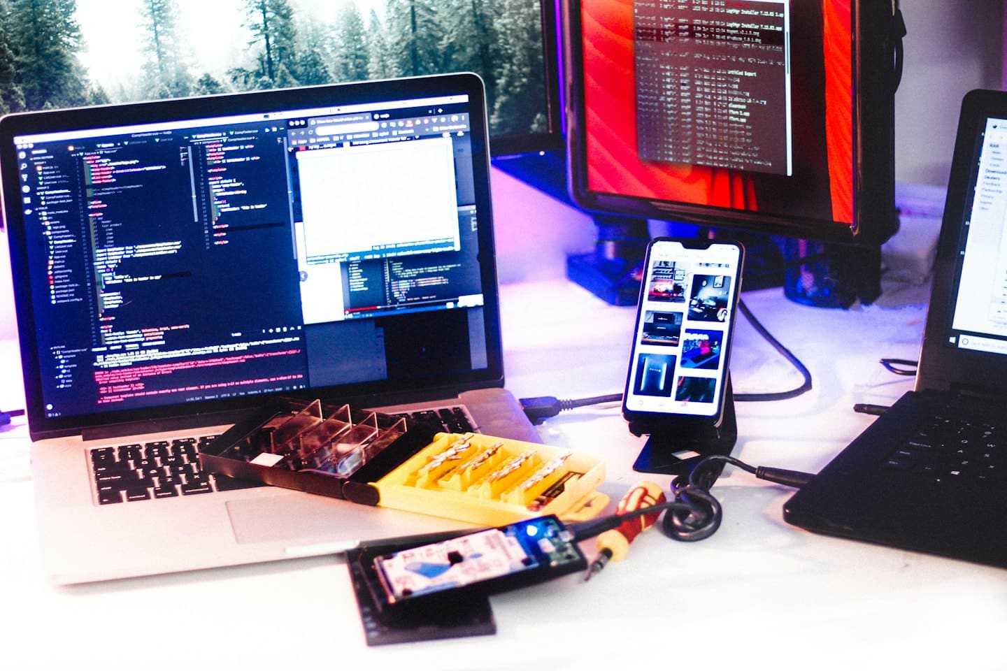 Tech workstation with a laptop displaying code and various cables.